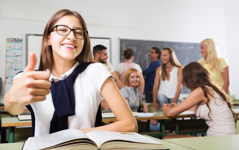 Estudiante en un salón de clases levantando el pulgar en señal de aprobación, simbolizando el éxito tras revalidar estudios