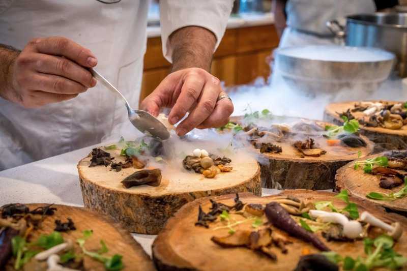 Chef elaborando un platillo con técnicas innovadoras sobre troncos de madera - Alta cocina sostenible y creatividad culinaria