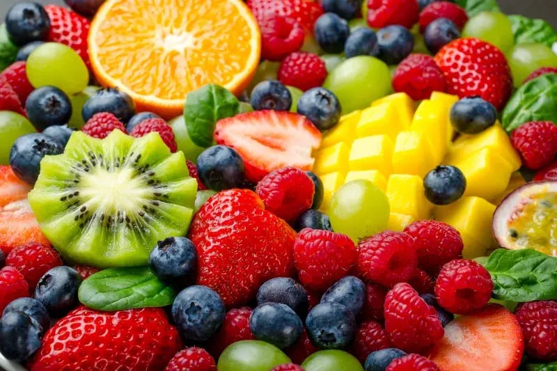 Frutas frescas coloridas como kiwis, fresas, uvas y mangos, representando alimentos ricos en nutrientes.