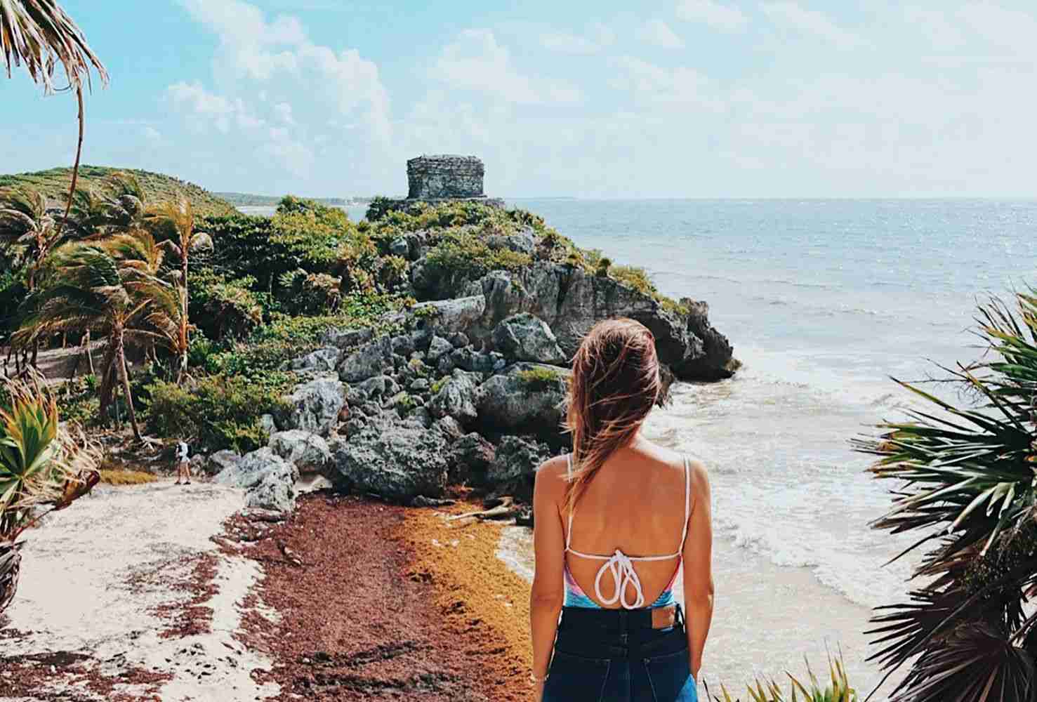 urista explorando las ruinas mayas de Tulum con vista al mar Caribe, un destino clave en los fam trips para la promoción turística.