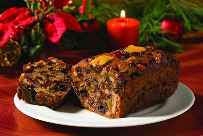 Panqué navideño de frutas y nueces con un fondo de velas rojas y decoración navideña.