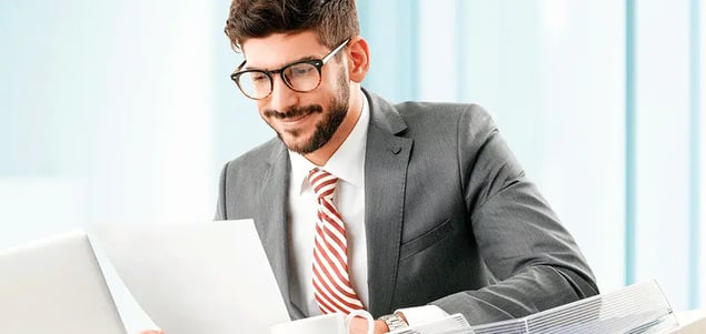 Hombre con traje y lentes, sonriendo mientras lee unos documentos