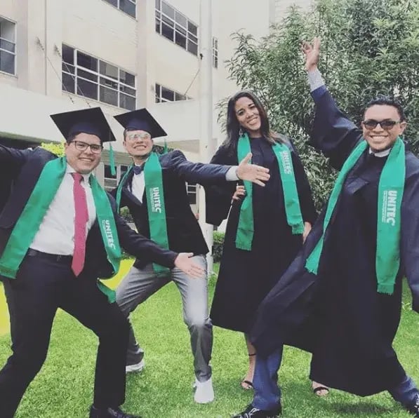 Graduados UNITEC con estolas verdes celebrando su logro académico en el campus.