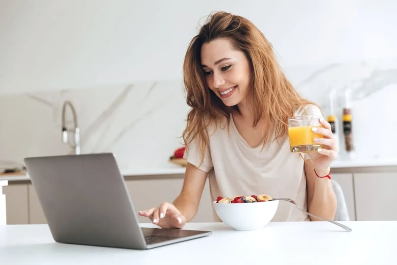 Mujer desayunando en su hogar tomando clases en línea motivada