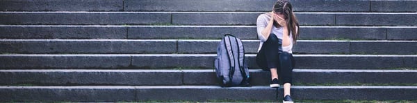 Estudiante universitaria con estrés sentada en escaleras, mochila al lado, simbolizando el impacto emocional de los exámenes.