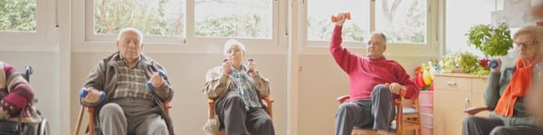 Adultos mayores realizando ejercicios con pesas en una sesión de fisioterapia geriátrica grupal, promoviendo movilidad y fuerza muscular.