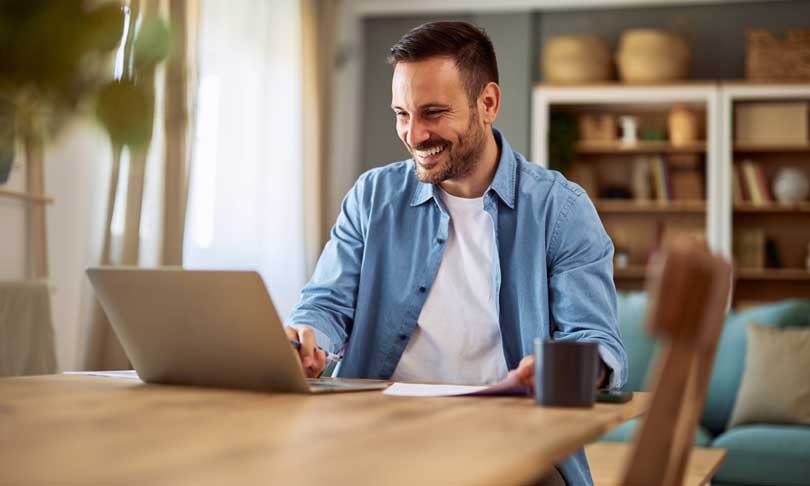 Hombre freelance sonriente leyendo comentarios positivos mientras cursa una maestría en línea de UNITEC desde su hogar.