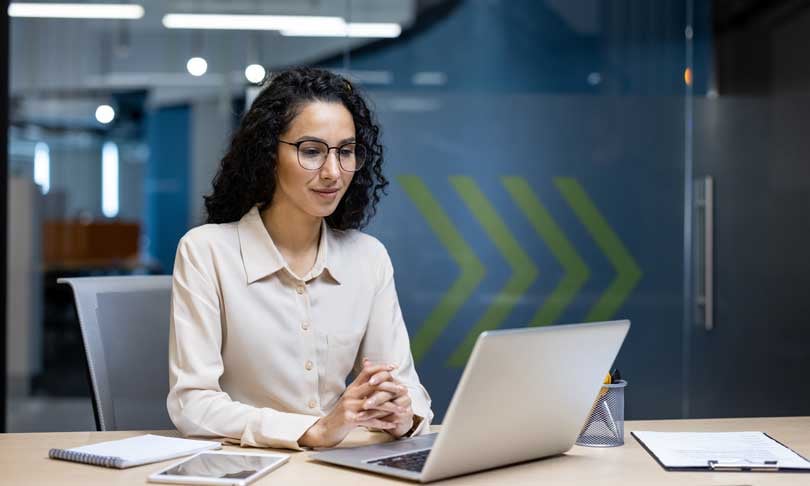 Mujer de negocios concentrada en su computadora mientras estudia una maestría en línea de Unitec en una oficina moderna.