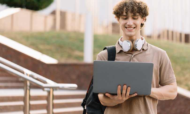 Hombre joven tomando notas mientras estudia en su computadora portátil desde casa, ejemplificando el aprendizaje a distancia y el estudio en línea.