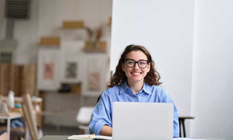 Joven empresaria feliz trabajando en su computadora portátil en un espacio moderno, reflejando la comodidad y flexibilidad de estudiar una licenciatura en línea