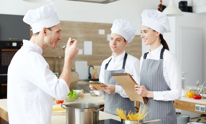 Chef evaluando platillo junto a estudiantes de gastronomía durante práctica en cocina profesional