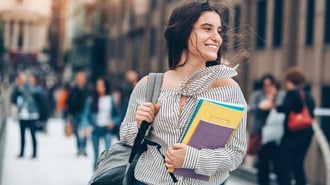 Estudiante feliz caminando con libros y mochila en un campus universitario. Satisfacción al elegir una carrera adecuada a intereses y metas personales.