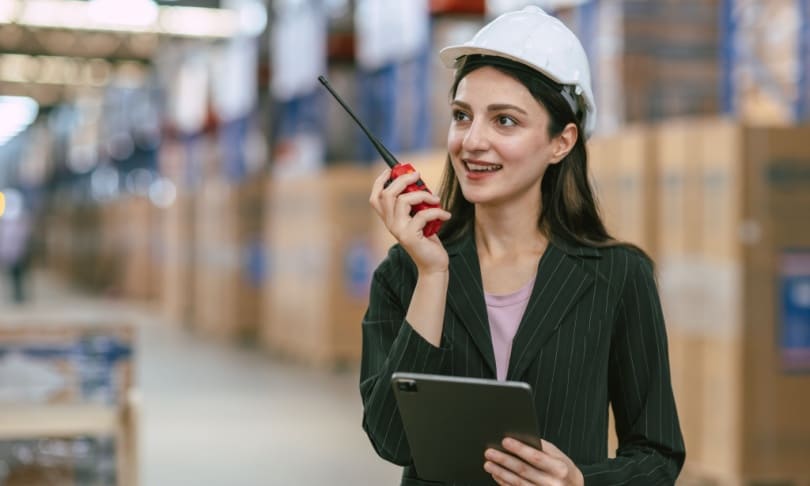 Ingeniera en logística supervisando operaciones de almacén con radio y tablet