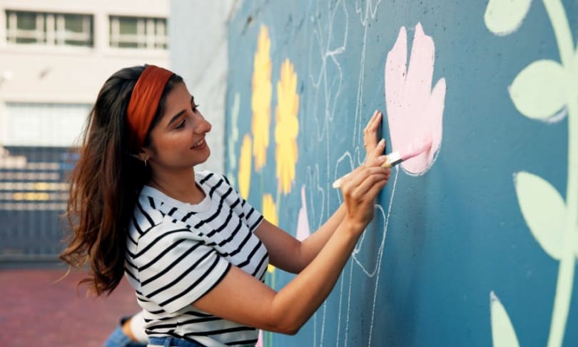 Mujer joven pintando un mural de flores, representando creatividad, pasión artística y elección vocacional basada en habilidades creativas.