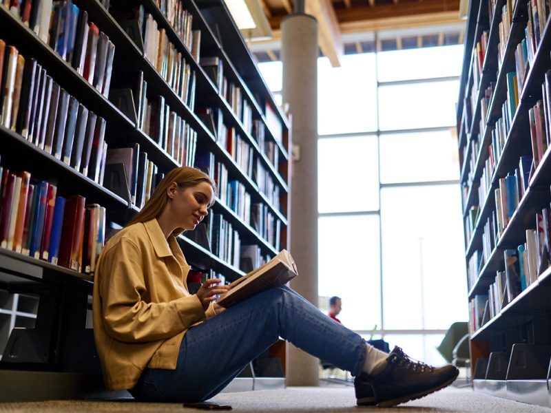 Estudiante con estilo de aprendizaje visual leyendo un libro en la biblioteca universitaria