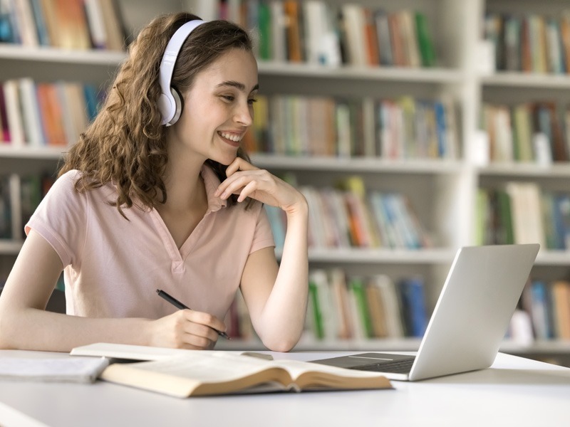 Mujer estudiante estudiando una licenciatura en línea desde biblioteca con laptop